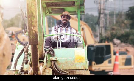 African worker driving heavy construction equipment backhoe with smile and happy Stock Photo