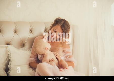 Mother and child on a bed. Mom and baby boy playing in bedroom. Parent and little kid relaxing at home. Family having fun together. Bedding and textil Stock Photo