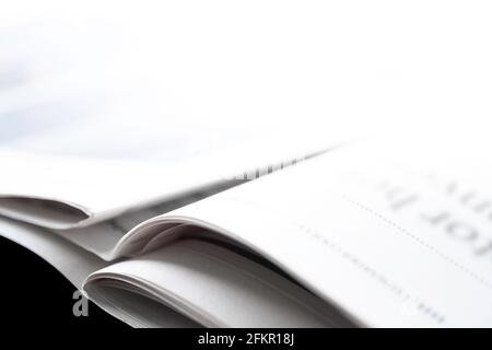 Open folded newspaper with unreadable headline lies diagonally on a black table. Photographed from a low point of view, very shallow depth of field Stock Photo