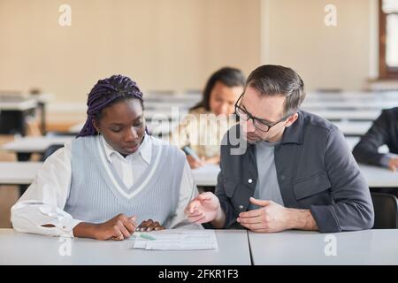 Portrait of mature professor helping African-American woman studying in college auditorium, copy space Stock Photo