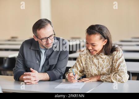 Portrait of smiling mature professor helping young African-American woman studying in college auditorium, copy space Stock Photo