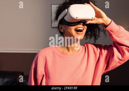 Exciting young woman in casuals wearing VR goggles indoors Stock Photo