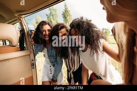Group of friends on road trip laughing at van. Young people standing together and having fun at minivan door. Stock Photo