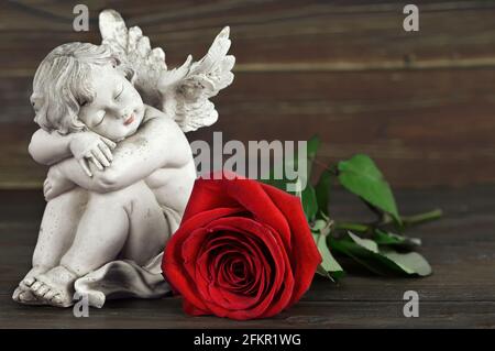 Little angel sleeping. Angel and red rose on wooden background Stock Photo