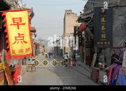 A street in Pingyao, Shanxi Province, China and Pingyao Tea House. A man is outside selling food and people walk in the street. Stock Photo