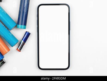 Recycling of batteries background with mobile phone mockup on white table, workspace top view Stock Photo