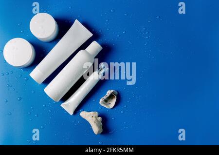 White cosmetic tubes for moisturiser, for cream for the care of the eyelids, closed jars for cream, bottle for lotion, myceular water on a blue backgr Stock Photo