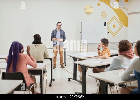 Wide angle view at mature male teacher giving lecture to class of young students in modern school, copy space Stock Photo