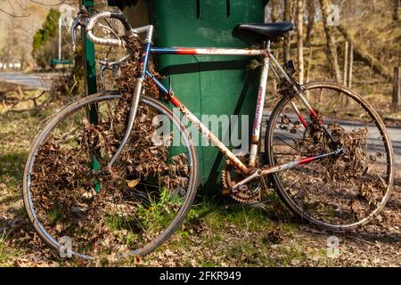 An old rusty bicycle leaning against a green bin Stock Photo