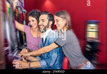 Happy young friends having fun together with slot machine - Gambling concept with people playing at cash automatic devices in modern casino and resort Stock Photo