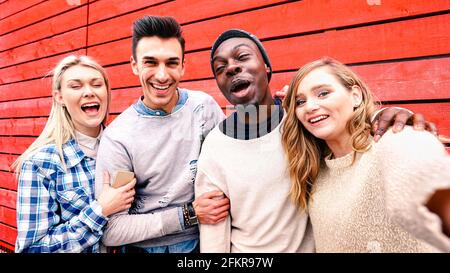 Happy multiracial friends taking group selfie at red wood background - Millenial people sharing fun stories on social media community Stock Photo