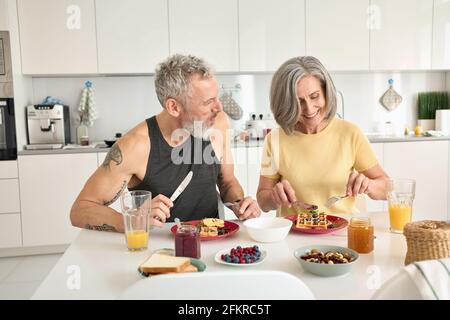 Happy healthy fit mature family couple having breakfast sit at kitchen table. Stock Photo