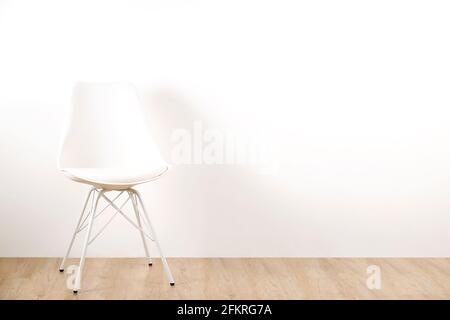 Single elegant white loft style chair standing alone on wooden floor in empty room, big blank wall background. Large copy space for text. Only one vac Stock Photo