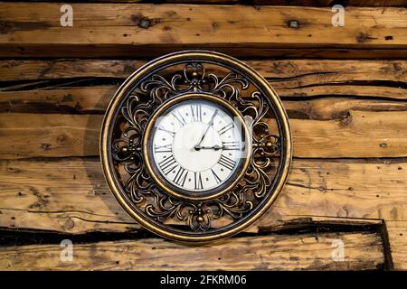 A round copper clock of the nineteenth century hangs on the wooden wall of an old house Stock Photo