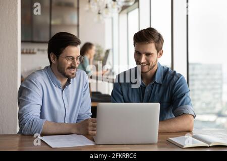 Smiling male colleagues cooperate together on laptop Stock Photo
