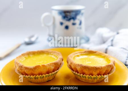 Egg tarts on a yellow plate with a cup of tea. Stock Photo