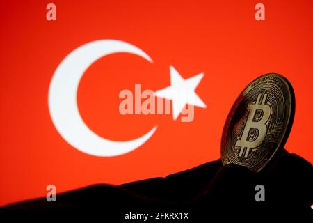 Bitcoin currency coin seen hold in silhouette of hand and Turkish flag on the blurred background. Concept. Stock Photo