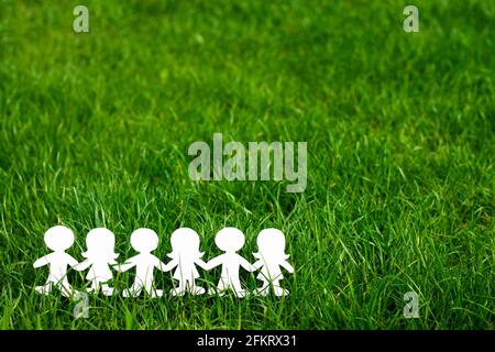 Silhouettes of children holding hands cut out of cardboard on a background of grass. Girls and boys made of white paper. International children's day. Stock Photo