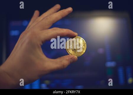 A man holds a gold bitcoin coin in his hand. The graphs of chang Stock Photo