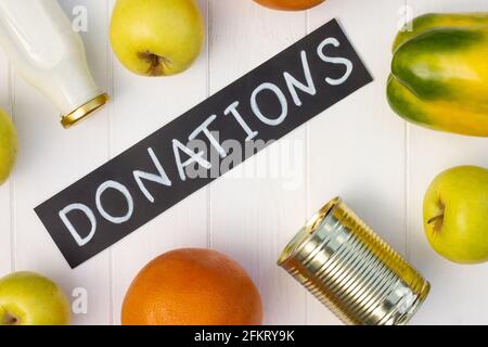 Cereals, canned food, milk, vegetables and fruits with a chalk Donations sign on a white wooden table. Flat lay. Charity and donation concept. Stock Photo