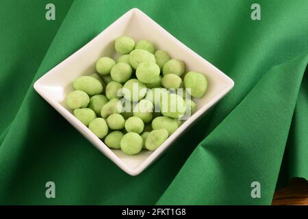 Wasabi covered and flavored peanuts in white snack bowl on green fabric Stock Photo