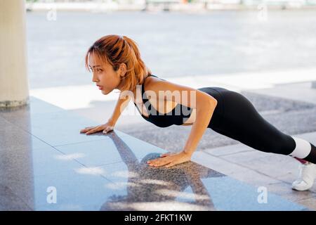 Sporty young Asian female athlete doing pushups in park in the park. Woman exercising in morning in sportswear Stock Photo