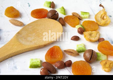 Dried fruits and nuts, apricot, almond, hazelnut pear prune and macadamia with bamboo wooden spoon on white background. Stock Photo