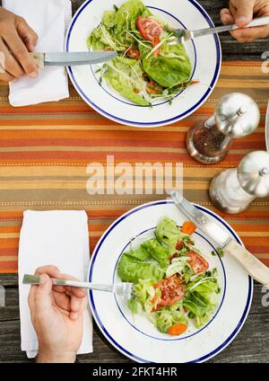 Overhead of the hands of father and son eating salad at table Stock Photo