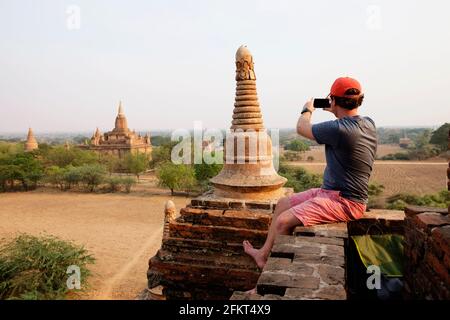 Man taking photograph from stone wall, Bagan Archaeological Zone, Buddhist temples, Mandalay, Myanmar Stock Photo