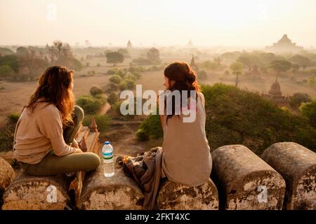 Women relaxing on stone wall, Bagan Archaeological Zone, Buddhist temples, Mandalay, Myanmar Stock Photo