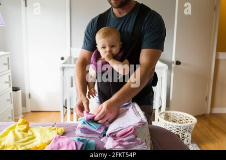 Mid adult man doing chores with baby daughter in baby sling Stock Photo