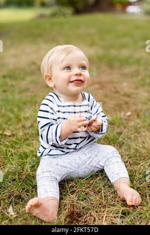 Portrait of baby girl sitting on grass, smiling Stock Photo