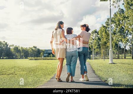 Three women friends with happiness emotion walking in the park hugging each otjher and smiling joyful. Stock Photo