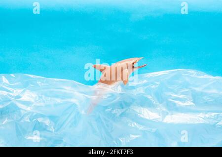 A dolphin toy model trapped in white plastic bag on blue background. Minimal ocean world concept. Stock Photo