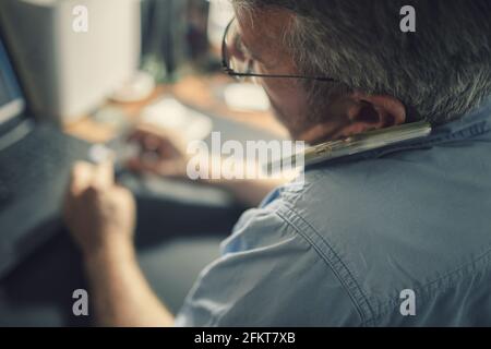 A senior man sitting at a desk in front of a laptop computer Stock Photo