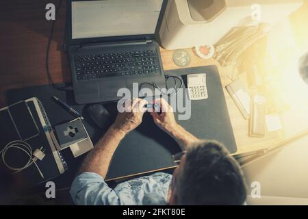 A senior man sitting at a desk in front of a laptop computer Stock Photo