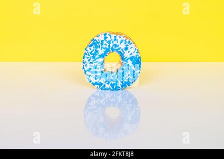 Donut with blue and white sprinkles on yellow background with reflection and copy space for text. Stock Photo