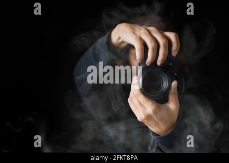 Woman's hands held photo camera. Close up shot. A person in black hoodie and smoke around Stock Photo
