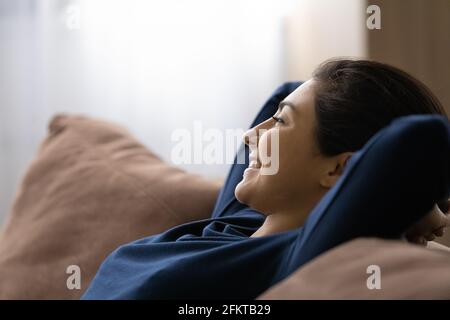 Close up smiling dreamy Indian woman relaxing on couch Stock Photo