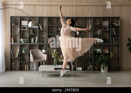 Overjoyed Indian woman wearing dress dancing, jumping in living room Stock Photo