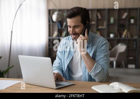 Smiling businessman talking on phone, using laptop, sitting at desk Stock Photo