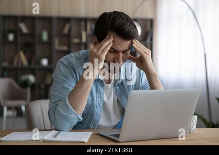 Upset businessman touching temples, suffering from strong headache at workplace Stock Photo