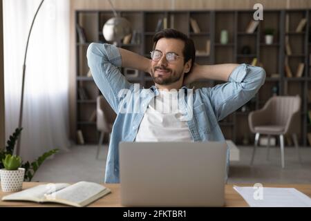 Positive dreamy businessman in glasses sitting at desk with laptop Stock Photo