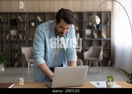 Confident businessman in glasses working on laptop, standing at desk Stock Photo