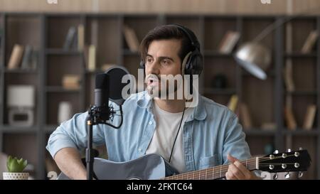 Close up man in headphones playing guitar, singing in microphone Stock Photo