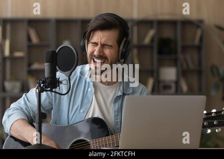 Close up man in headphones singing in microphone, playing guitar Stock Photo