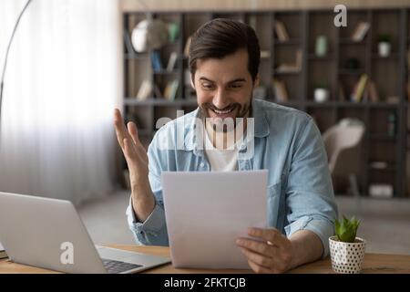Excited businessman reading good news in letter, sitting at workplace Stock Photo