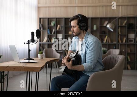 Confident man in headphones playing guitar, looking at laptop screen Stock Photo