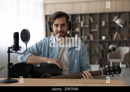 Portrait man in headphones holding guitar, sitting in home studio Stock Photo