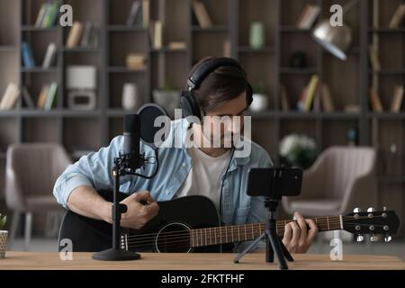 Man in headphones playing acoustic guitar, recording video on smartphone Stock Photo